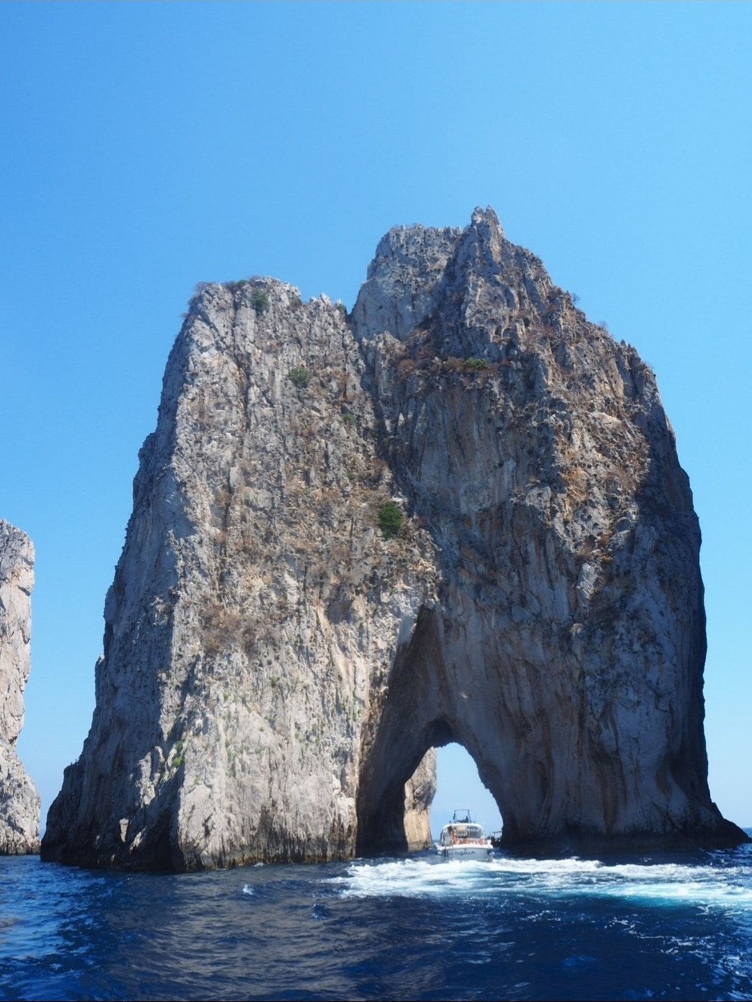 A boat passing through the Faraglioni arch