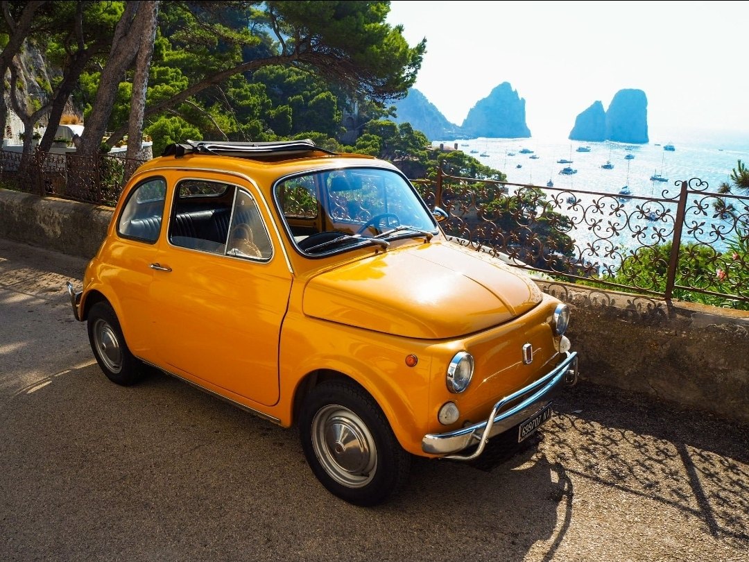 A yellow Fiat 500 with the Faraglioni behind