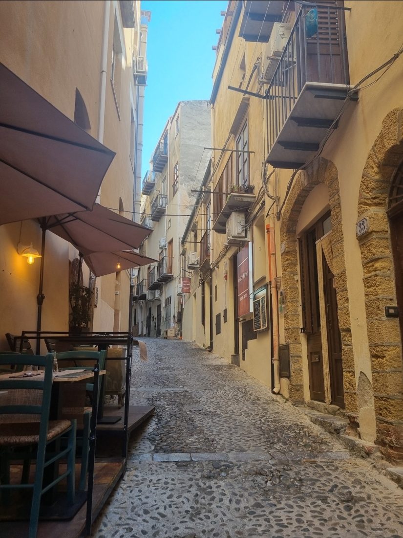 A narrow cobbled lane and a restaurant terrace in Cefalù